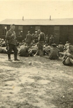 Fotografia „Obóz jeniecki żołnierzy radzieckich na Bukówce, 1942 r.”, przedstawia drewniane baraki i niemieckiego żołnierza pilnującego grupę radzieckich jeńców,