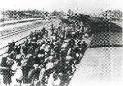 Więźniowie po opuszczeniu wagonów na rampie kolejowej w Auschwitz II-Birkenau, w dali widoczne kominy krematoriów II i III, b.d. [ze zbiorów APMAB].